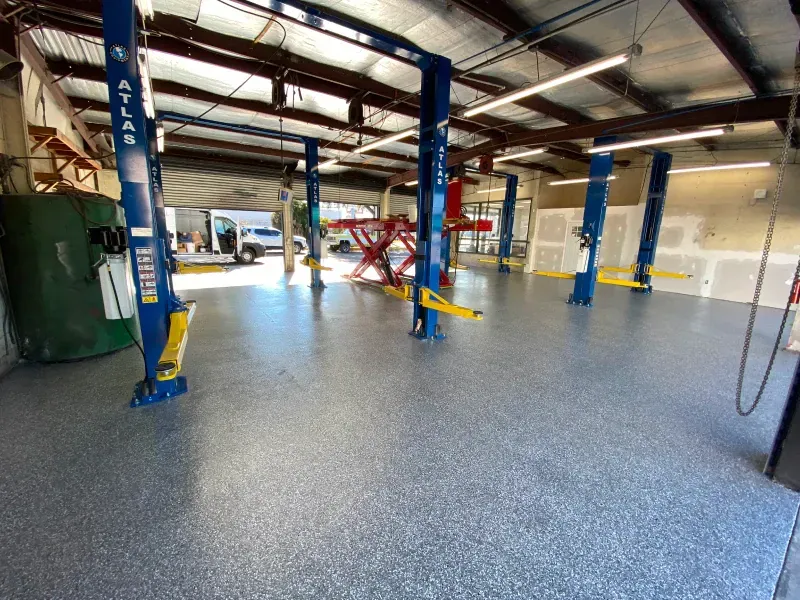 An auto repair shop with a newly coated epoxy floor, car lifts, and a vehicle visible through an open bay door.
